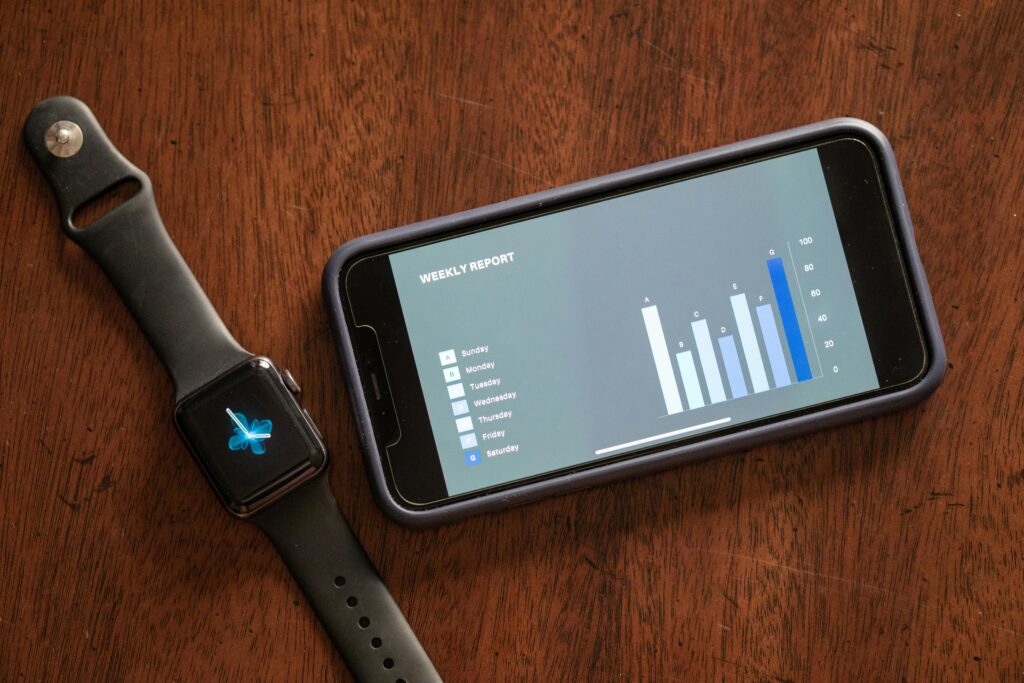 A smartwatch with an animated butterfly next to a smartphone showing a weekly report graph on a wooden table.