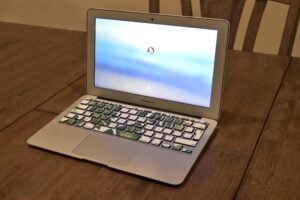 **Alt Text:** An open MacBook Air with a blurred login screen sits on a wooden table.
