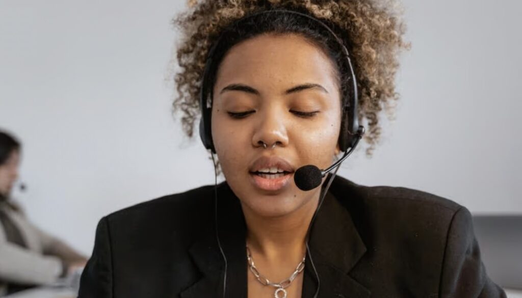 A person wearing a headset with a microphone appears to be speaking or listening with eyes gently closed.