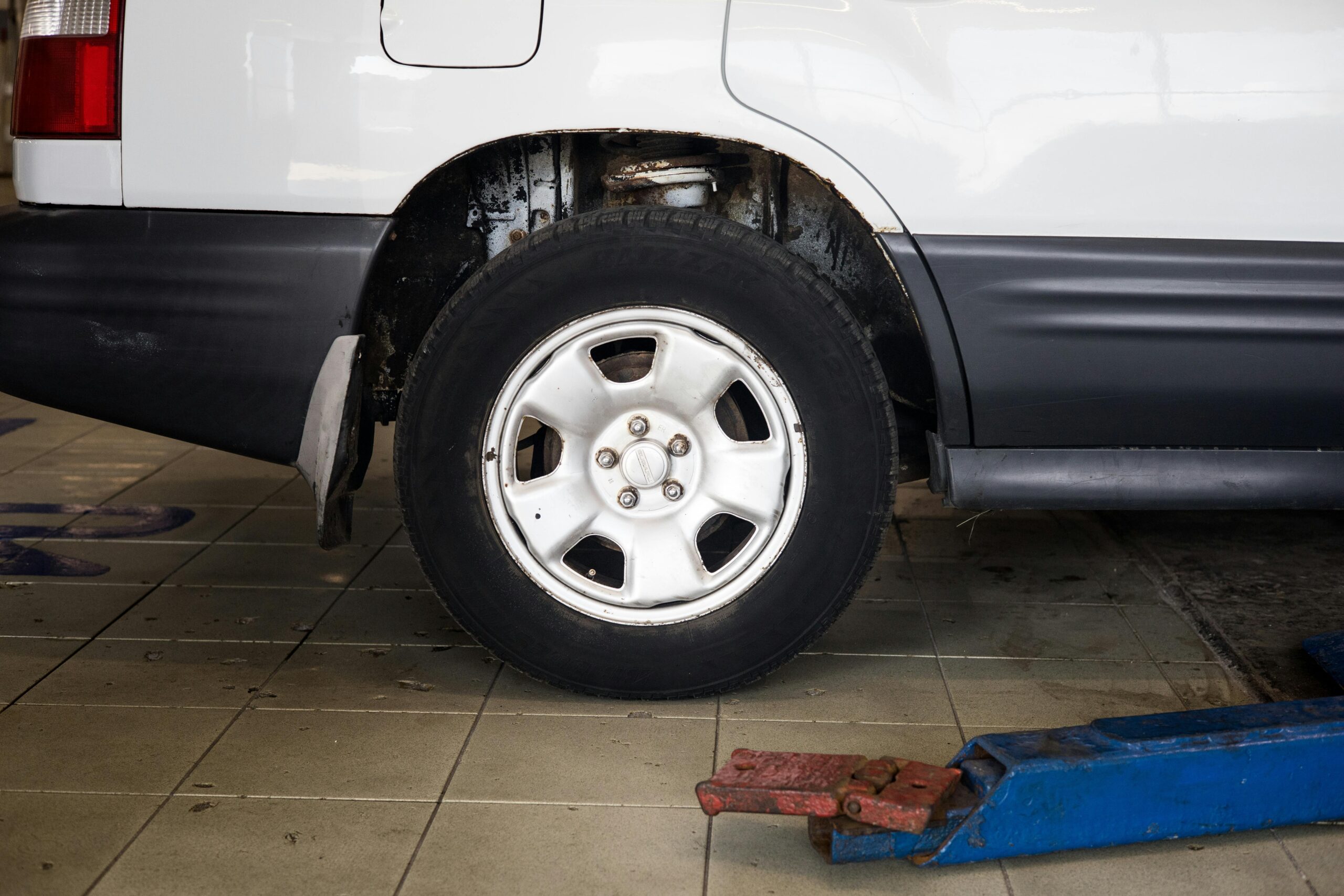 A car is positioned on a mechanical lift in a garage, showing its rear wheel and part of the vehicle's body.