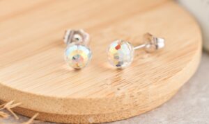 Two faceted stud earrings with iridescent beads are displayed on a wooden surface.