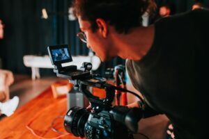 **Alt Text:** A person is intently looking at the display screen of a professional video camera on a film set.
