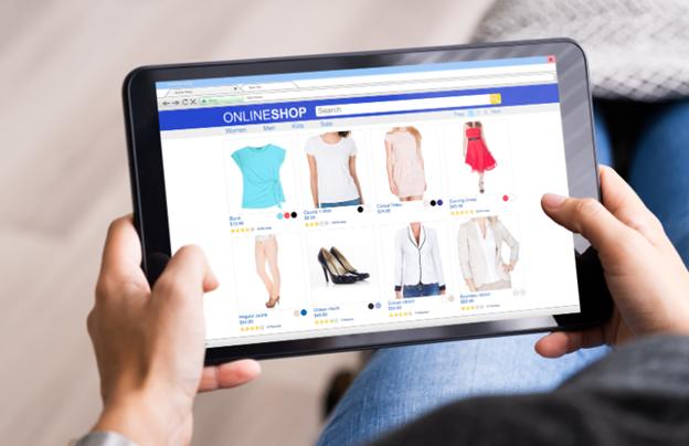 **Alt Text:** A person holding a tablet browsing an online clothing store displaying various shirts, dresses, and shoes.