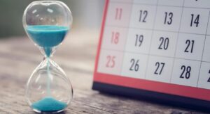 **Alt Text:** An hourglass with blue sand is placed next to a calendar displaying a month with weeks running from Sunday to Saturday.