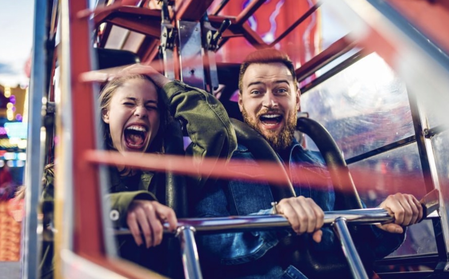 **Alt text:** A man and a woman with expressions of excitement and thrill are seated on a carnival ride.