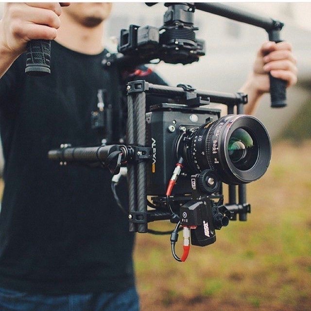 **Alt Text:** A person is holding a professional camera mounted on a stabilizing rig outdoors.