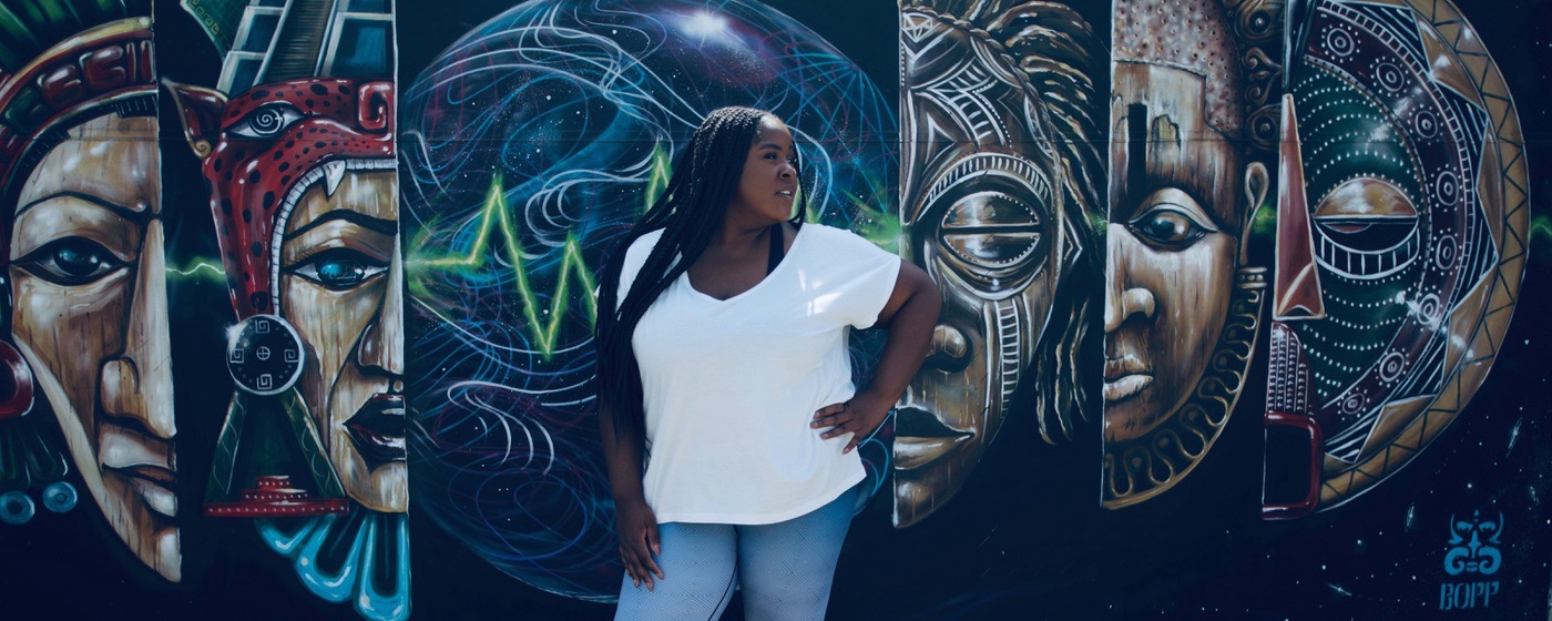 A person stands in front of a colorful mural featuring abstract and cultural designs.