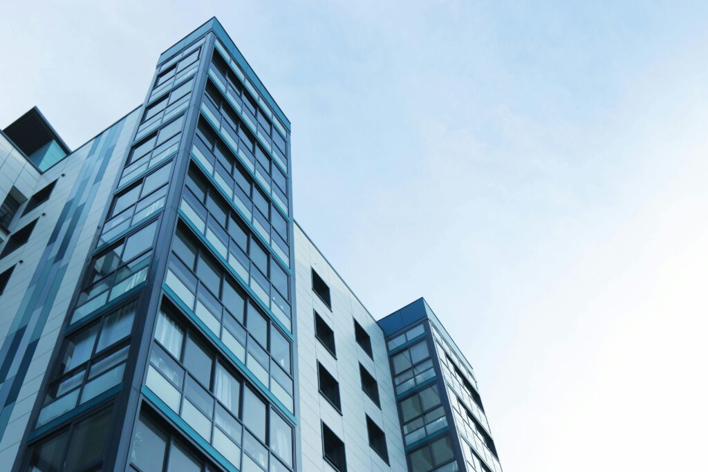 **Alt text:** A modern glass-fronted apartment building angled against a clear blue sky.