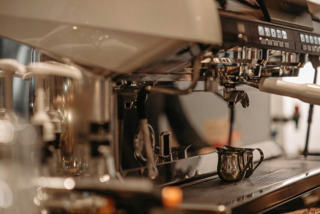 A close-up view of a professional espresso machine with a small metal pitcher placed on its tray.