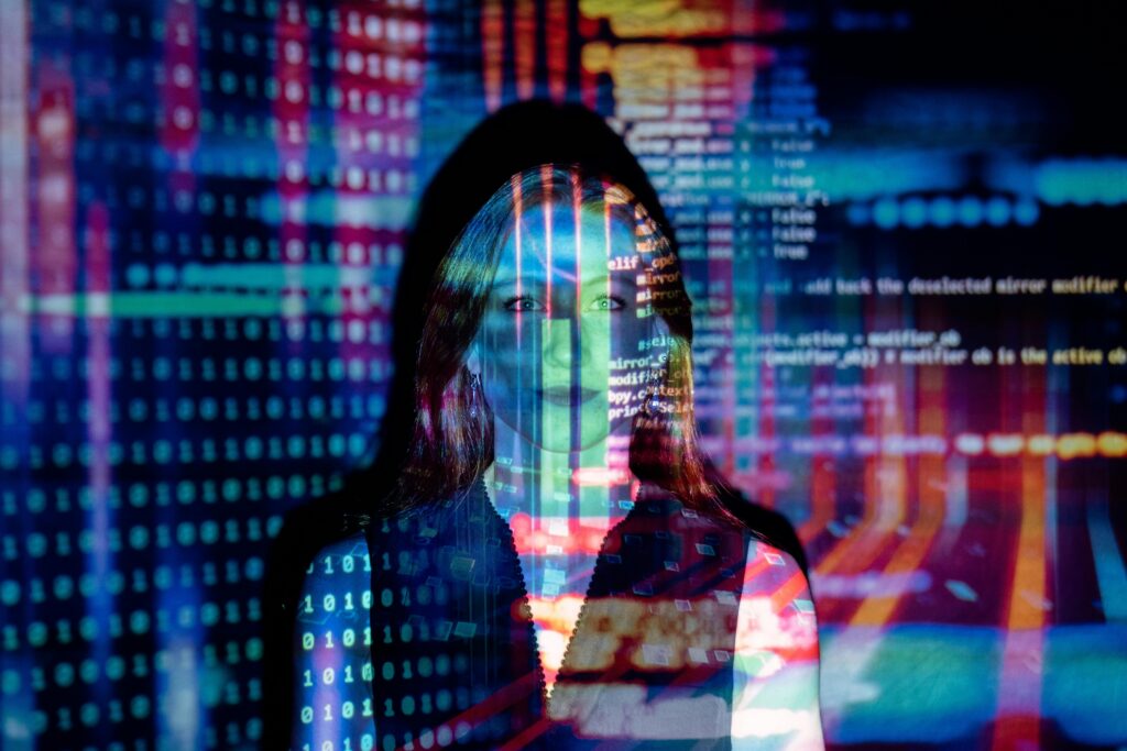 A person stands in front of a screen with colorful lines of code projected over their face and body.