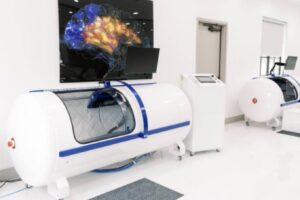 **Alt text:** A medical facility with two hyperbaric chambers, a control panel, and a digital display showing a brain image on the wall.