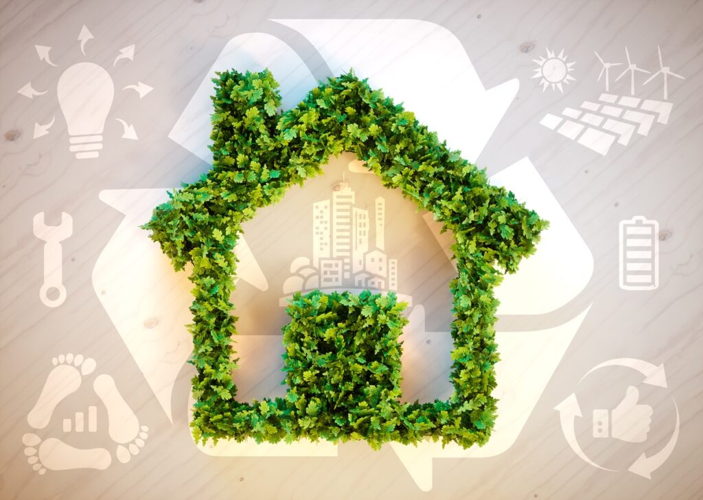 **Alt text:** A house shape made of green leaves sits on a wooden surface, surrounded by symbols of sustainability such as solar panels, wind turbines, and recycling.
