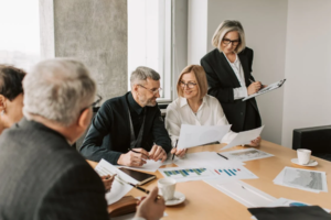 A group of business professionals collaborate around a conference table with documents and charts.