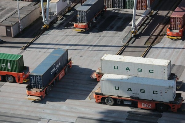 **Alt text:** Trucks transporting large shipping containers in a port facility.