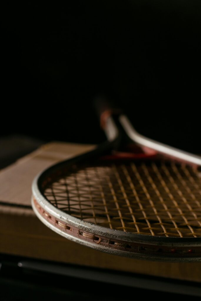**Alt text:** A close-up of a vintage tennis racket placed on a wooden surface in a dimly lit setting.