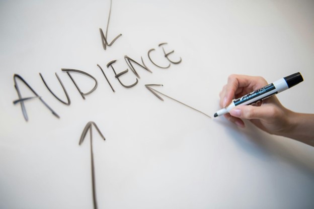 A hand writes the word "AUDIENCE" on a whiteboard with arrows pointing towards it.