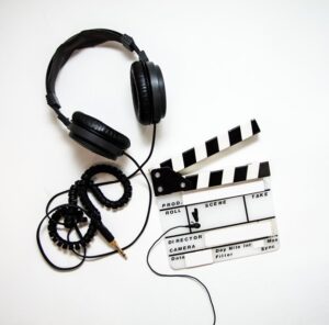 **Alt text:** Black headphones and a black-and-white film clapperboard are placed on a white surface.