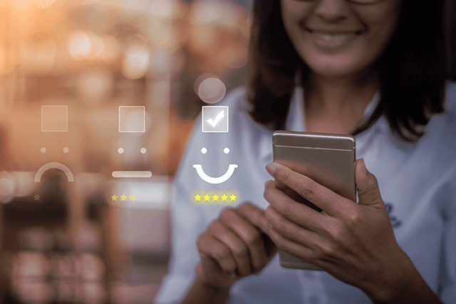 A woman holding a smartphone is selecting a happy face with five stars on a virtual feedback rating scale.
