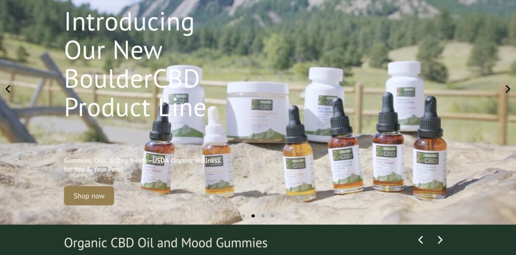 **Alt text:** Various BoulderCBD products, including tinctures and jars, are displayed outdoors with a mountainous background.