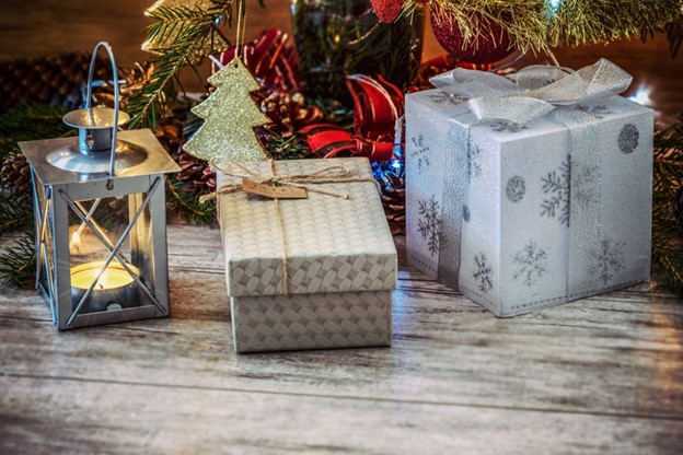 **Alt Text:** A cozy scene featuring a lit lantern, two wrapped gift boxes with Christmas decorations and a tree in the background.