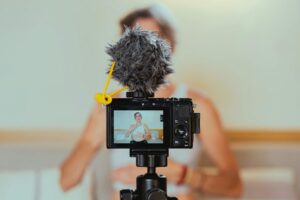 **Alt Text:** A camera with a fuzzy microphone records a person speaking in a room.