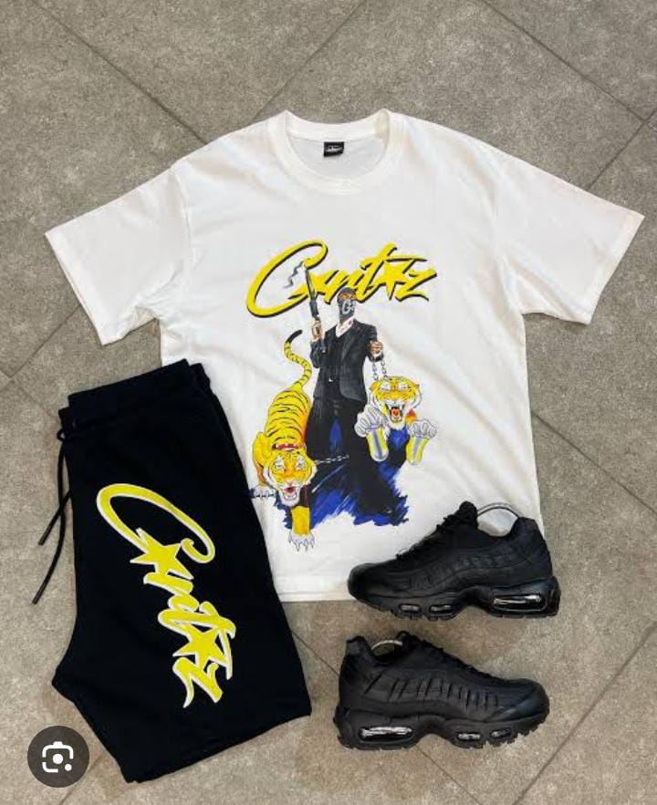 **Alt Text:** A white T-shirt with an illustrated design featuring a person in a suit and tigers, laid next to black shorts with yellow writing and a pair of black sneakers.