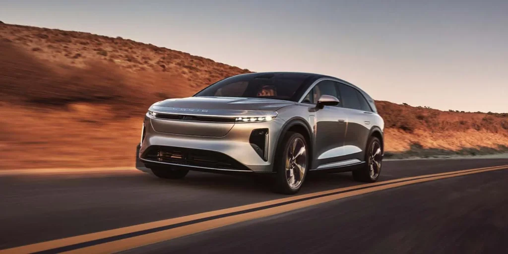 **Alt text:** A sleek silver electric SUV driving on a desert road at sunset.