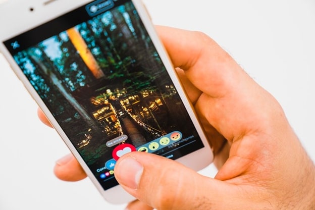 **Alt text:** A person holding a smartphone showing an image of a forest scene with digital reaction icons below.