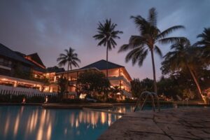 **Alt text:** A tropical resort with a pool and palm trees, illuminated at dusk.
