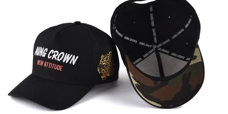 **Alt text:** Two black baseball caps are shown, one displaying "Aung Crown New Attitude" and a tiger embroidery, and the other revealing a camouflage pattern under the brim.