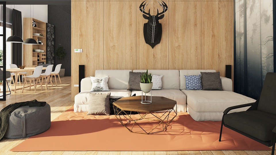 A modern living room with a white sectional sofa, decorated with various cushions, a wooden coffee table, a plant, and a wall-mounted deer sculpture, leading to a dining area with white chairs and wooden shelves.