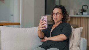 A woman sitting on a couch looking at her phone with a surprised expression.