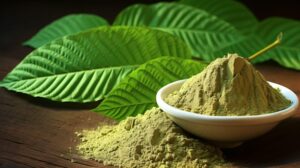 A bowl of green powder alongside several large green leaves on a wooden surface.