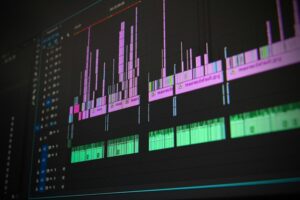 **Alt Text:** A close-up of a computer screen displaying a video editing timeline with multiple audio and video tracks in green and pink colors.