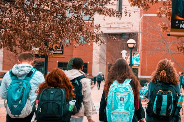**Alt text:** A group of students with backpacks walking towards a university building surrounded by trees.