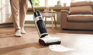 A person uses a vacuum cleaner to clean a spill of cereal and milk on a hardwood floor in a living room.
