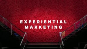 **Alt Text:** The image shows a red wall with the words "EXPERIENTIAL MARKETING" written in large white letters, flanked by two staircases.