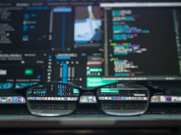 **Alt Text:** A pair of eyeglasses is placed in front of a laptop screen displaying colorful programming code and software interfaces, with the screen reflected in the lenses.