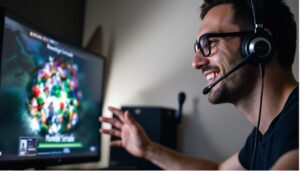 A man wearing glasses and a headset smiles while interacting with a colorful game on a computer screen.