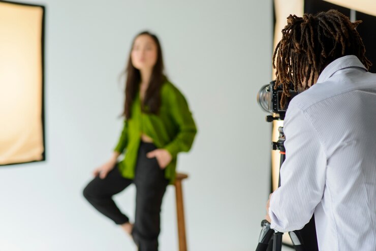 A photographer captures an image of a person in a green blouse sitting on a stool in a studio with soft lighting.