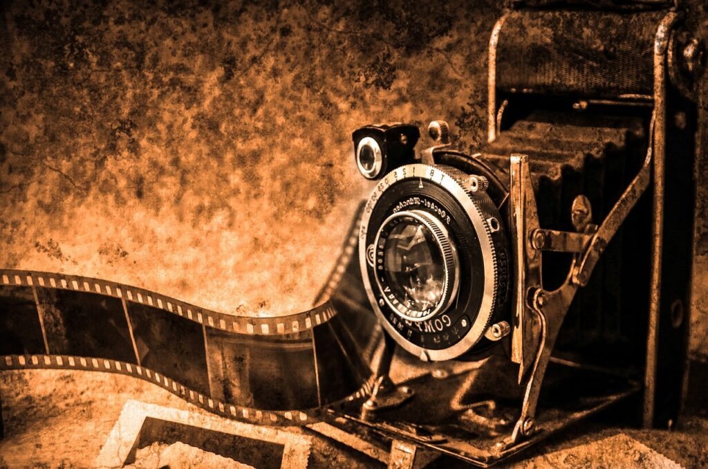 A vintage camera with extended bellows and a foldable design is positioned next to a roll of film against a textured, sepia-toned background.