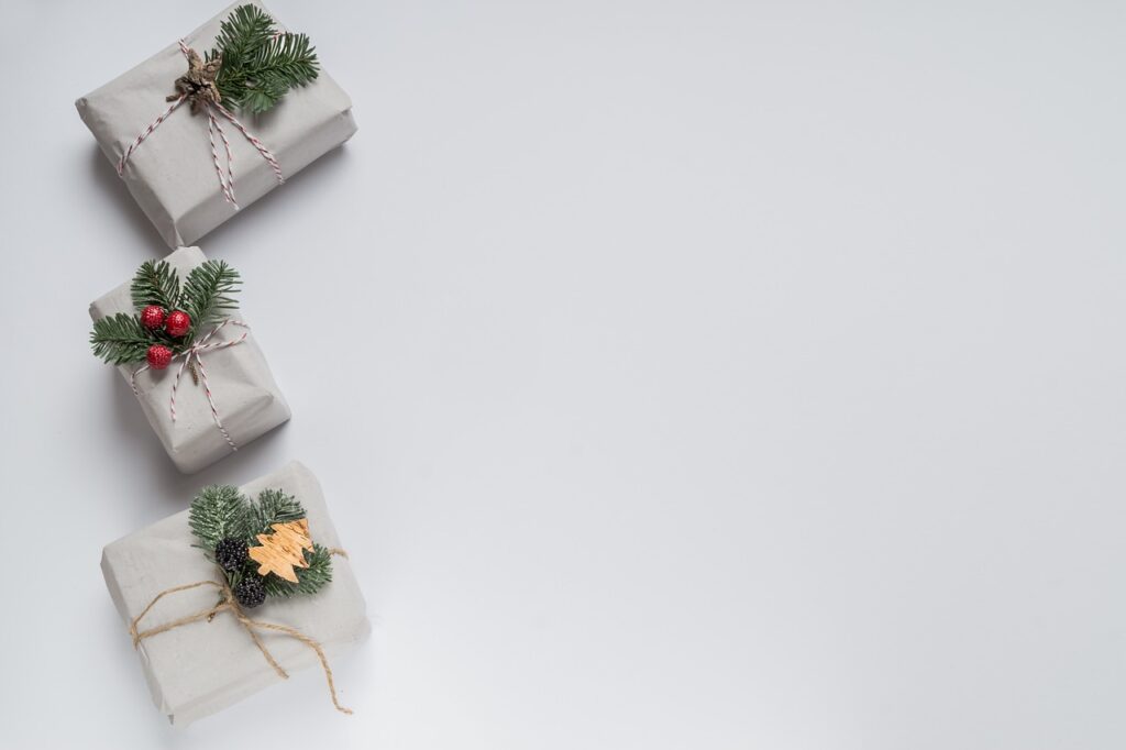 **Alt text:** Three gift boxes wrapped in plain paper with pine branch and berry decorations are positioned on the left side, leaving space on a white background.