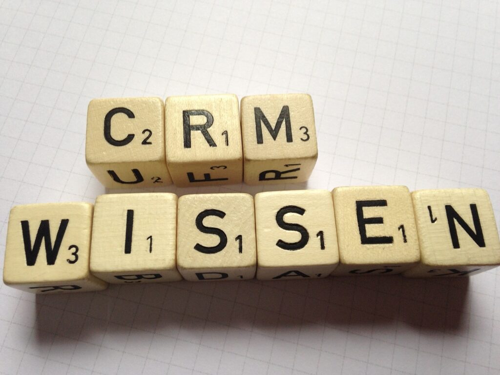 Wooden Scrabble tiles arranged to spell "CRM" and "WISSEN" on a grid-patterned paper.