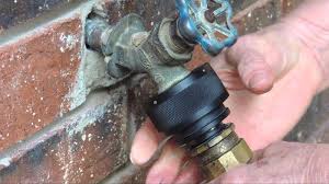 **Alt Text:** Hands installing a black anti-siphon device onto an outdoor faucet attached to a brick wall.