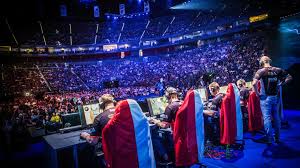 **Alt Text:** A team of gamers competes in an eSports tournament in front of a large audience in a stadium.
