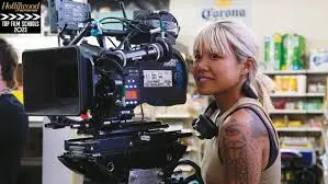 A woman with tattoos operates a professional film camera in a grocery store.