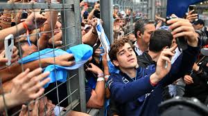 **Alt text:** A young man taking a selfie with fans who are reaching through a metal fence, some holding flags.