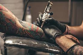 "Tattoo artist wearing black gloves works on tattooing a person's arm covered in colorful designs."