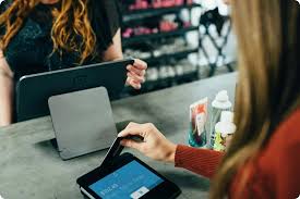 **Alt text:** A person swipes a credit card on a tablet-based payment terminal at a store counter.