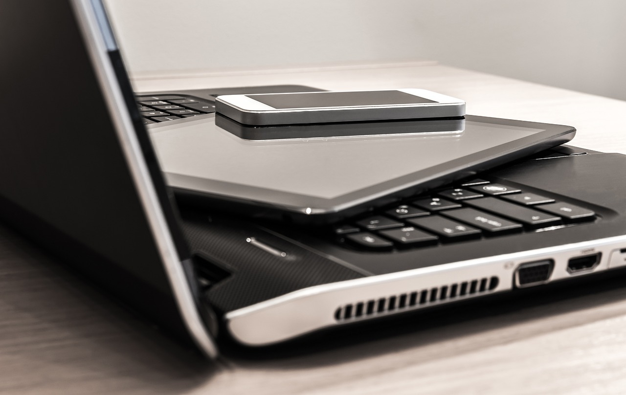 **Alt Text:** A smartphone and tablet are placed on top of a slightly open laptop.